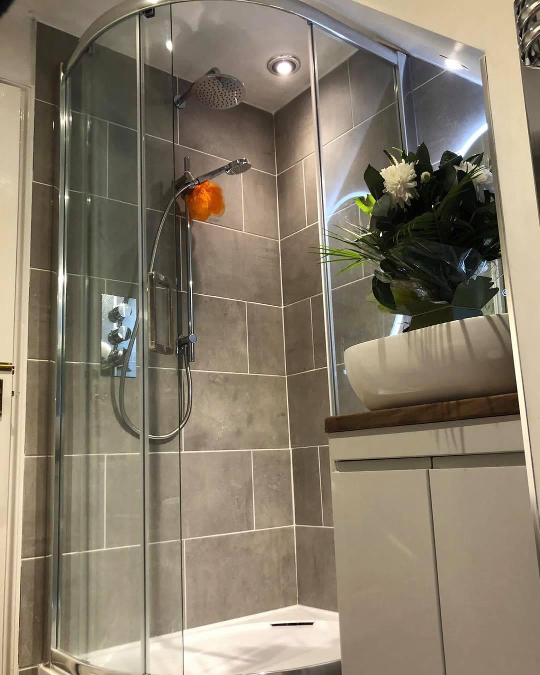 Shower enclosure in grey tiles beside a white vanity unit with a vessel basin