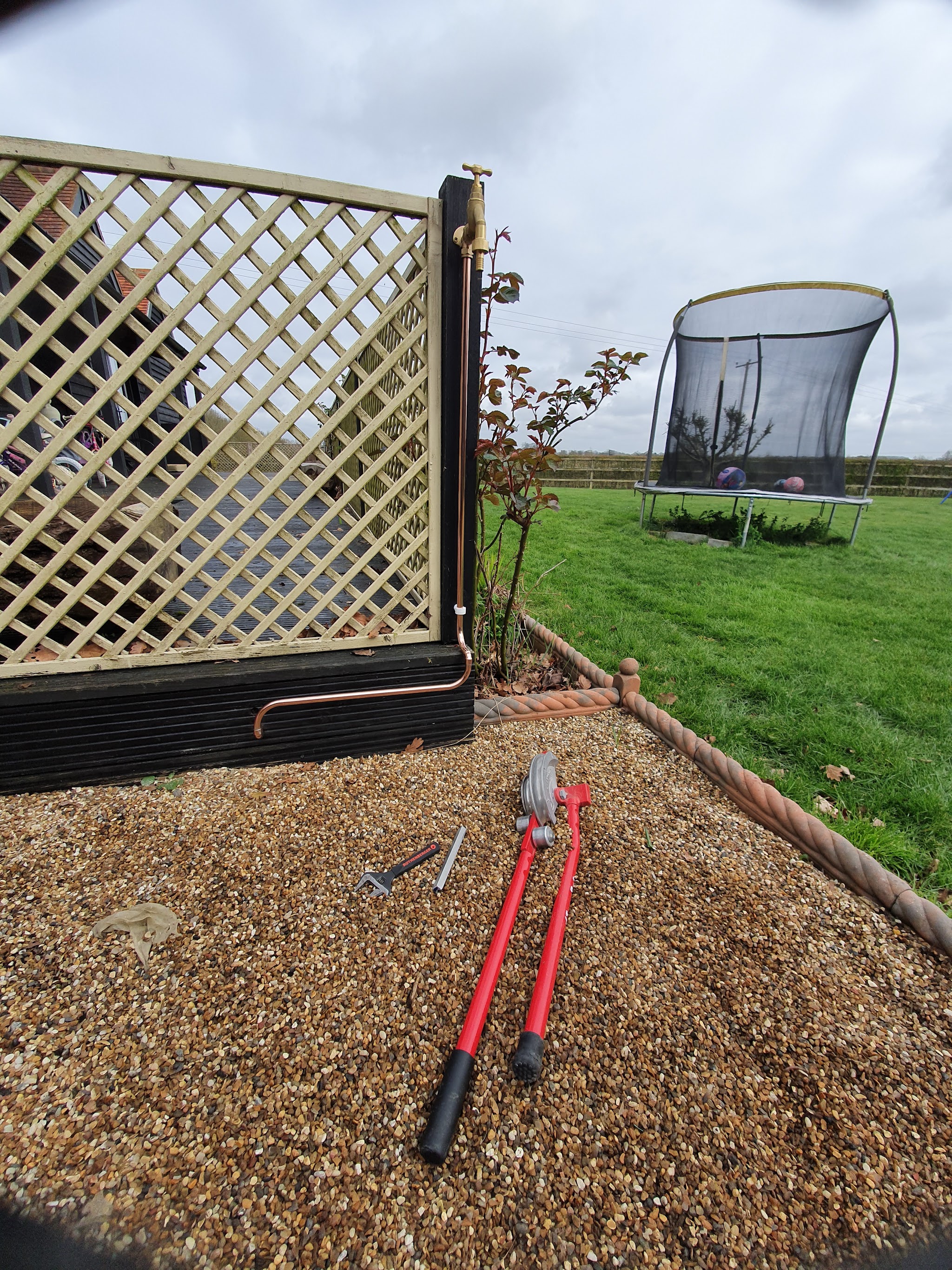 Copper pipework run along a garden fence, with bolt cutters on the gravel