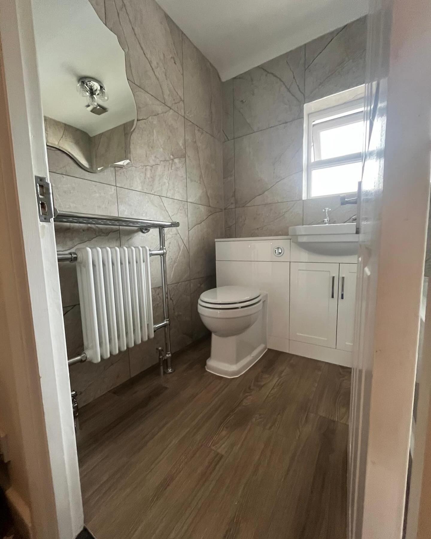 Compact bathroom with a column towel radiator, fitted vanity and toilet unit, and wood-effect floor